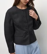 Blazer de sastrería color gris con estampado de cuadros, cuello redondo y cierre frontal con botones forrados. Presenta mangas largas con volumen tipo baloné y bolsillos frontales con solapa.