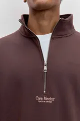 Buzo de cuello alto con cierre frontal parcial, de corte holgado y diseño minimalista con pequeño estampado central en el pecho.