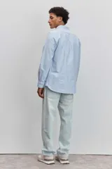 Camisa de manga larga en color celeste con estampado de rayas verticales finas, cuello abotonado y cierre frontal con botones.