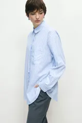 Camisa celeste con rayas verticales blancas, de corte oversize, manga larga y cuello clásico.