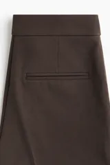 Pantalón de vestir color marrón oscuro, corte bootcut, con raya marcada en el frente y el reverso. Presenta pretina prolongada con cierre oculto y bolsillos al bies y ribeteados en la parte trasera.