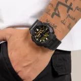 Reloj Casio G-Shock analógico-digital con caja robusta de resina y carbono, correa de resina negra y esfera negra con detalles en dorado. Cuenta con resistencia a impactos, múltiples funciones digitales y resistencia al agua de 200 metros.