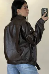 Chaqueta de ecocuero negro con diseño oversize, cuello solapa, cierre frontal y cinturón ajustable en el ruedo.