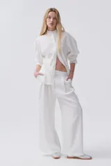 Pantalón de lino blanco, de pierna ancha, con pinzas en el frente, botón en la cintura y bolsillos laterales y traseros.