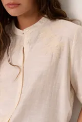 Camisa de manga corta color blanco con cuello mao y cierre frontal de botones. Presenta detalles bordados tono sobre tono en el canesú y diseño de corte recto.