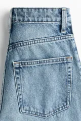Jean tobillero de denim de algodón rígido, de tiro alto y diseño curvo con volumen en las piernas. Presenta cinco bolsillos, cierre de cremallera y botón, pinzas en las rodillas y costuras laterales avanzadas.