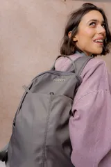 Mochila compacta de color beige, con compartimento principal con cierre, bolsillos laterales y bolsillo frontal con cierre oculto. Cuenta con correas regulables y acolchonadas y asa superior.