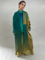 Tapado largo de lana merino afieltrada con diseño de paneles en degradé de tonos verdes y ocres. Presenta hombros caídos, mangas rectas, bolsillos laterales y cierre frontal con broches ocultos.