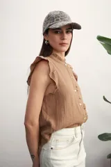 Camisa color amarillo pálido con textura arrugada, cuello mao con volados, cierre frontal con botones y mangas cortas con volados.