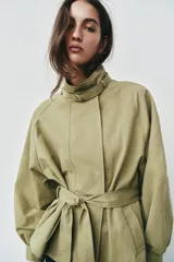 Cazadora de color verde militar, con cuello alto, manga larga abullonada con puños y cierre frontal con botones a presión ocultos. Incluye un cinturón ajustable del mismo tejido para entallar la cintura y bolsillos delanteros de vivo.