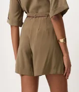 Short suelto color bordó con pinzas frontales, bolsillos laterales y cierre con cremallera y botón. Incluye cinturón fino de rafia con hebilla metálica.