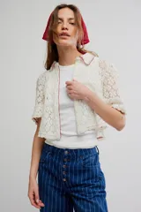 Camisa crop de encaje floral semitransparente, color blanco, con mangas cortas y ribetes en color contrastante.
