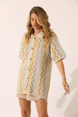 Vestido corto color crema con cuello tipo polo, mangas cortas y cierre delantero con botones. Diseño con patrón de zigzag en tonos celeste, naranja y lila.