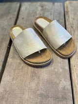 Sandalias con base marrón y tira ancha de cuero color dorado.