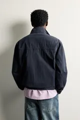 Cazadora tipo canguro de corte regular fit en tejido técnico ligero color azul marino, con cuello subido, cierre frontal parcial con botones a presión y bolsillos de vivo en la cadera. Cuenta con acabados elásticos en puños y cintura.