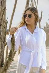 Camisa blanca de manga larga con cuello clásico, ajuste en la cintura mediante lazo del mismo tejido y hombros ligeramente abullonados.