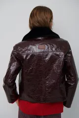 Chaqueta de efecto cuero brillante con acabado charol, cuello con solapas de piel sintética, cierre frontal con botones y bolsillos laterales.