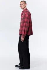 Camisa de sarga de algodón con diseño a cuadros, cuello inglés, bolsillo en el pecho y cierre frontal de botones. Presenta mangas largas con puños abotonados y bajo redondeado.