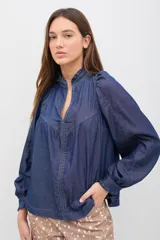 Camisa de denim azul con costuras a la vista en color contrastante, cuello camisero, mangas largas abullonadas con puños abotonados y corte holgado.