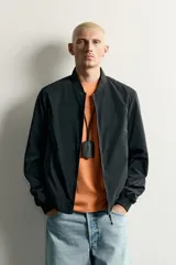 Cazadora bomber de tejido técnico ligero color marrón oscuro, con corte regular fit, cuello, puños y ruedo de rib elástico, bolsillos frontales de vivo y cierre frontal con cremallera.