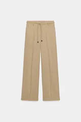 Pantalón de tiro medio color beige con sutiles rayas verticales blancas, de corte recto y amplio. Cuenta con bolsillos delanteros y un cinturón trenzado del mismo tejido con cordón ajustable.