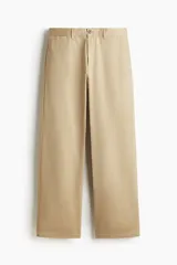 Pantalón chino color beige, de corte relajado, confeccionado en sarga de algodón. Cuenta con cierre frontal de botón, bolsillos al bies y bolsillos traseros ojetes con botón.