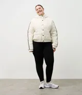 Campera puffer deportiva Get Over, color blanco con detalles de bies en color negro a lo largo de las mangas. Presenta cuello alto con capucha integrada, cierre frontal con botones a presión, bolsillos laterales con cremallera y puños con elásticos.