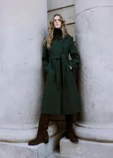 Abrigo largo de paño en color verde oscuro, con cuello alto, cierre frontal oculto y cinturón ajustable del mismo tejido. Presenta un diseño estructurado con bolsillos laterales.