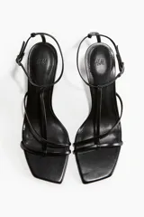 Sandalias negras de tacón fino con punta cuadrada y tiras finas sobre el empeine. Pulsera ajustable con hebilla de metal.