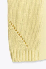 Jersey de punto color amarillo pálido, con cuello redondo y mangas cortas. Presenta un calce oversize y aberturas caladas en los laterales inferiores.