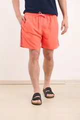 Short de baño color coral con cintura elástica ajustable con cordón y detalle de ribete azul marino en los laterales.