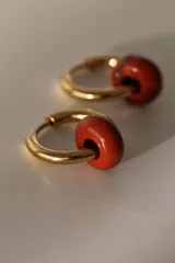 Par de aros tipo argolla dorados de acero quirúrgico, con una piedra natural de color gris translúcido colgando de cada uno.