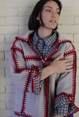 Chaqueta reversible de paño, con un lado gris oscuro con costuras decorativas en hilo rojo y el otro lado con estampado de cuadros. Presenta corte holgado, mangas largas y diseño abierto.