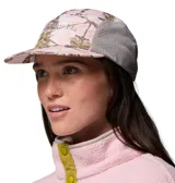 Gorro tipo gorra Columbia modelo Wingmark Cap, con paneles laterales de malla gris y diseño estampado camuflado en tonos rosados y blancos en el frente y la visera. Cuenta con logo bordado de la marca.