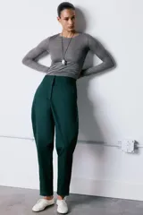 Pantalón de tiro alto confeccionado en mezcla de algodón, con diseño de volumen y costuras torcidas. Presenta bolsillos laterales y cierre frontal con cremallera, botón interior y ganchos metálicos ocultos.