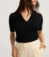Blusa negra de punto con cuello polo, escote en V y mangas cortas. Detalle de mini perlas aplicadas en el cuello.