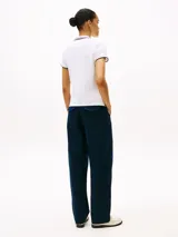 Chomba blanca de corte slim fit, confeccionada en algodón elástico. Presenta cuello y mangas con ribetes en azul y rojo, tapeta de cinco botones y logo de Tommy Hilfiger bordado en el pecho.