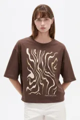 Remera de manga corta de algodón en color blanco, con cuello redondo y diseño holgado. Presenta un estampado frontal con detalle de acabado metálico (foil).
