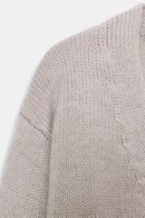 Chaqueta de punto color beige, confeccionada en 100% lana, con escote en pico, manga larga y cierre frontal con botones.