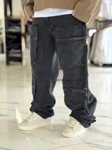 Pantalón cargo de jean negro con efecto acid wash, corte oversize, tiro medio y múltiples bolsillos laterales con solapa y cierres colgantes.