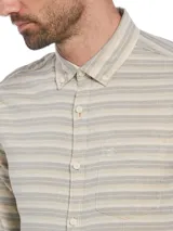 Camisa de hombre de manga larga con rayas horizontales en tonos beige y gris. Tiene cuello abotonado, bolsillo en el pecho y cierre con botones.