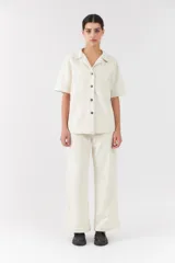 Conjunto de dos piezas color blanco off-white, compuesto por una camisa de manga corta con cuello camisero y bolsillos frontales, y un pantalón largo de corte recto y holgado.