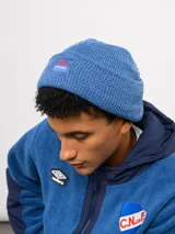Gorro tipo beanie de tejido de punto color blanco crema, con parche frontal que incluye el logo de Umbro y la inscripción Nacional.