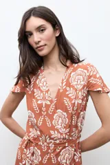 Vestido corto cruzado de color terracota con estampado floral blanco, escote en V, mangas cortas con vuelo y volados en el borde de la falda y la abertura.