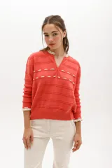Sweater de punto color coral con rayas horizontales y detalles calados. Tiene escote en V con lazo y ribetes con volados en cuello y puños. Confeccionado en algodón egipcio.