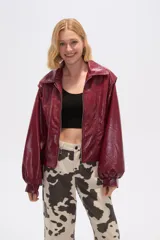 Chaqueta corta de cuero sintético negro con cuello camisero, cierre frontal con cremallera, bolsillos laterales y mangas largas abullonadas.