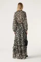 Vestido largo de gasa color negro con estampado floral blanco, escote en V cruzado, mangas largas con aberturas en los hombros y falda con volantes.