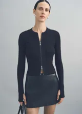 Chaqueta de punto fino color negro, con diseño entallado, cuello redondo, manga larga y cierre frontal con cremallera completa.