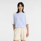 Remera New Balance de algodón con diseño de mangas raglán en color blanco y cuerpo en color lila. Presenta cuello redondo y un gráfico bordado con el nombre de la marca en el centro del pecho.