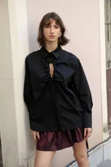 Camisa oversize de manga larga en color blanco, confeccionada en algodón. Presenta cuello clásico, puños abotonados y una abertura central ovalada con jaretas ajustables que permiten fruncir la prenda.
